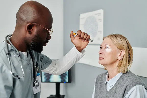 In a medical office, a male ophthalmologist uses a pen light