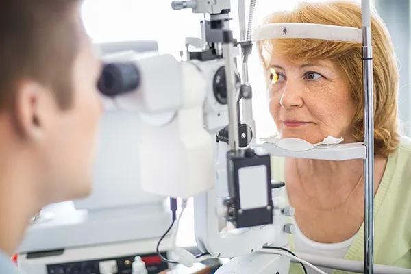 A woman with ginger hair sits behind a slit lamp while havin