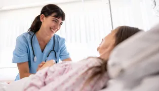 Woman in scrubs taking care of woman in hospital bed