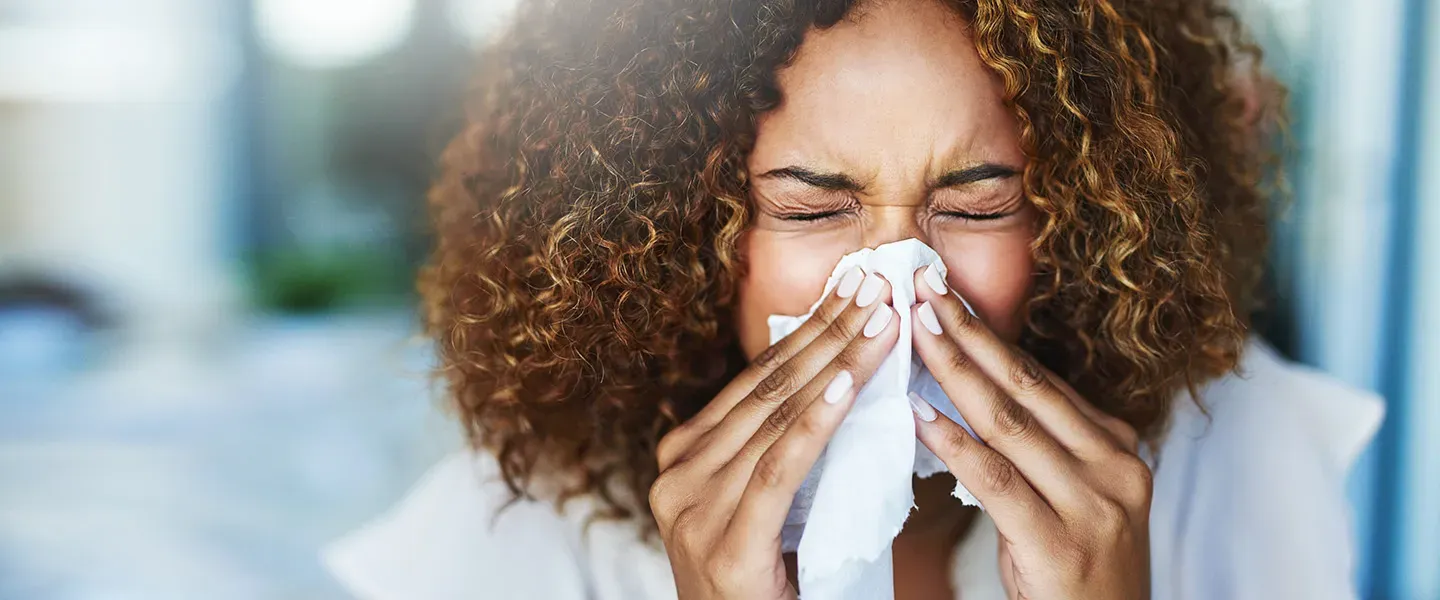 A woman has clogged sinuses and blows her nose using a tissu