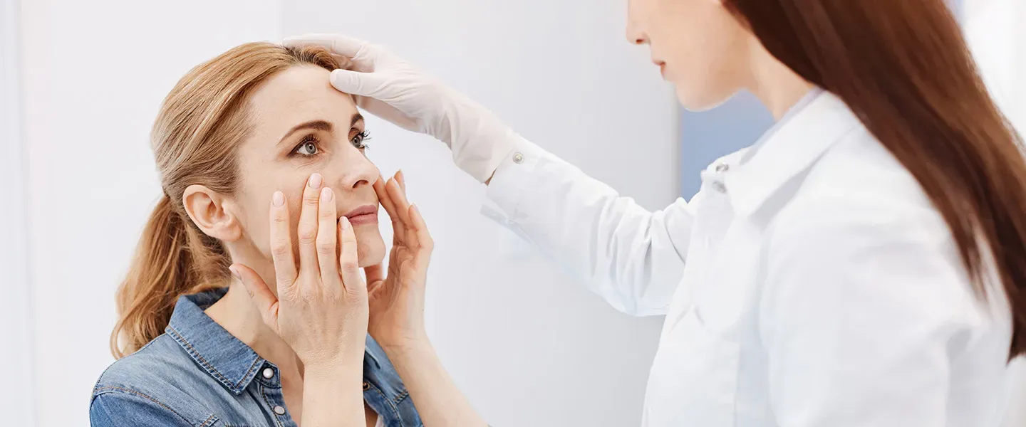 A concerned woman touches her face while being examined by a