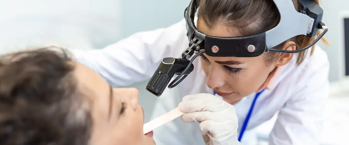 A doctor examines a patient's throat using a light and a ton