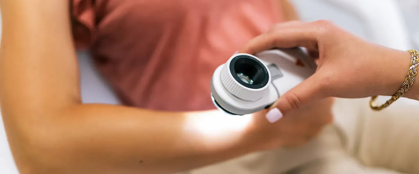 A doctor examines a patient's arm using a loupe.