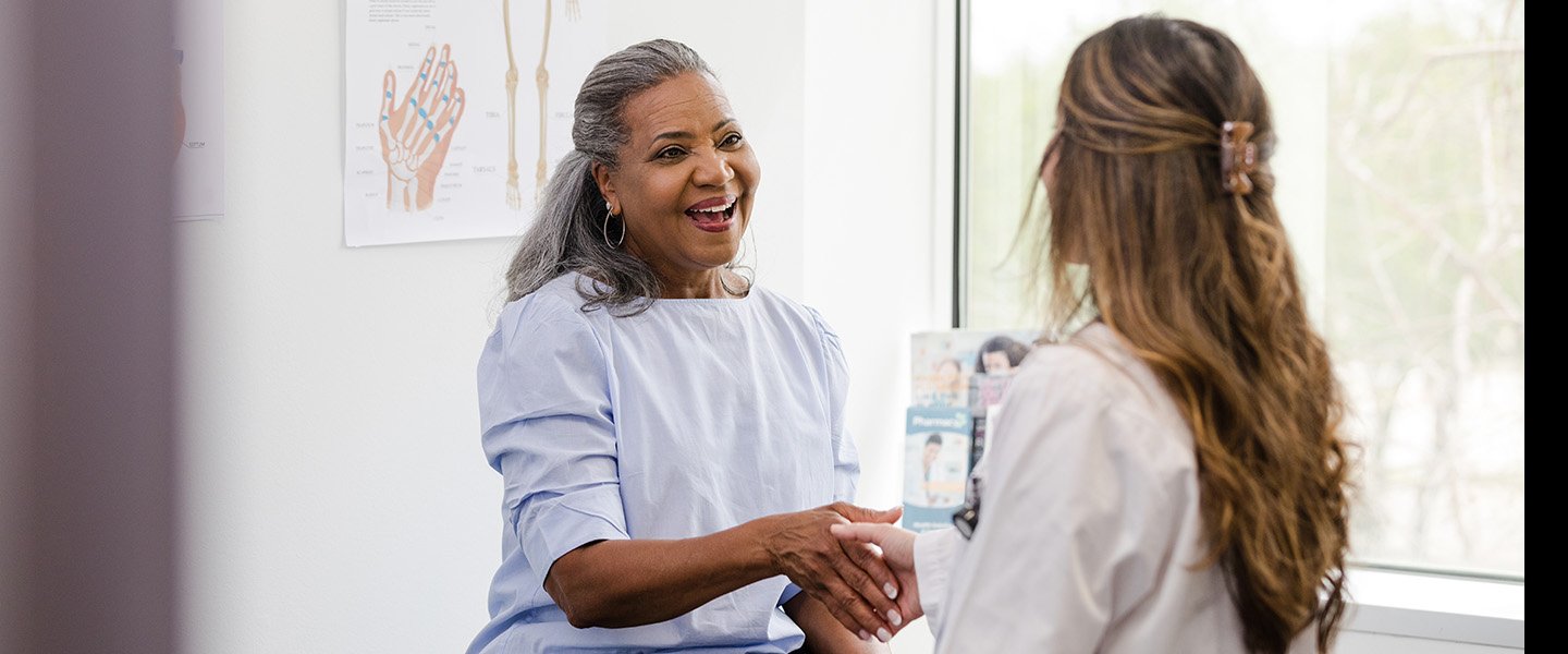 A female patient and female doctor shake hands and talk in a
