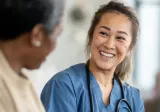 A female nurse sits with a senior patient with stethoscope o