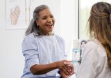 A female patient and female doctor shake hands and talk in a