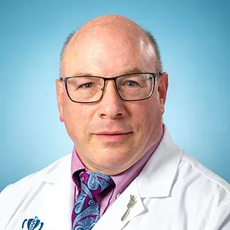 Dr. Berney is wearing glasses and a purple shirt with blue p