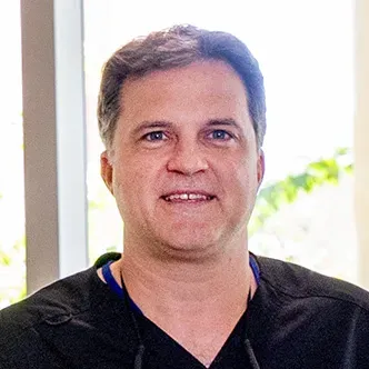 Dr. Bak has short dark hair, is wearing black surgical scrub