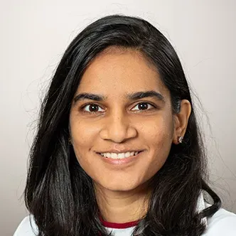 Dr. Desai has long dark hair, is wearing a white medical coa