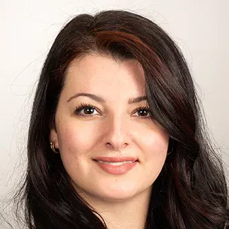 Dr. Jasim has long, dark, wavy hair, is wearing a white blou