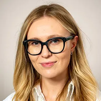 Dr. Kovalenko has long blonde hair, is wearing black rimmed 