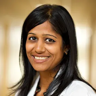 Dr. Patel has long, straight dark hair, is wearing a white m