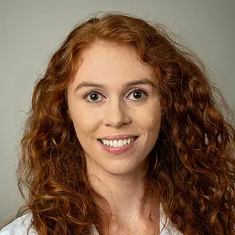 Daniella Schneider has long curly red hair, is wearing a whi