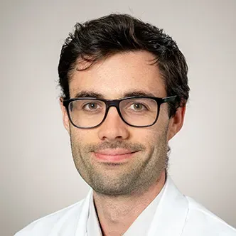 Dr. Thomson has short dark hair and glasses, a short beard, 